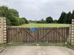A field surrounded by fencing and closed off with two gates and a sign reading 'Please keep clear, access required at all times'.