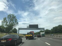 Driving on a busy four-lane motorway, with a gantry across the road.