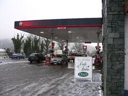 Cars parked under a Texaco-branded filling station, with snow on the ground. A sign says The Bridge Cafe Bistro Open.