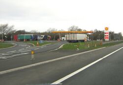 A slip road leading in to a forecourt with Shell signs outside it.