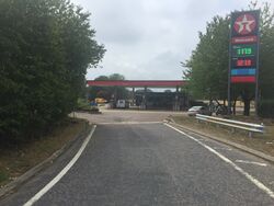 Road leading into a Texaco forecourt, with a branded sign on the right.