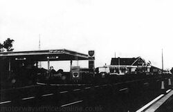 A black and white photo of a BP-branded petrol station next to a main road, with another building in the distance.