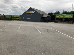 A building, painted black, with the Subway logo, next to a car park.