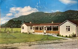 Old colour picture of a bungalow in front of a mountain.