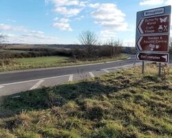 A road sign for Wroughton pointing down a road next to a field.