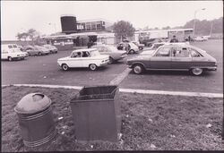 Black and white view of cars parked outside the service area building.