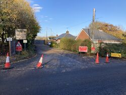 A short length of road with houses along it; cones are placed across the entrance and various road signs say, 'private property', 'no parking for McDonalds customers', 'road closed' and 'diverted traffic to the right'.