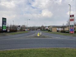 The exit from the roundabout with a sign for the Co-op on the left, and a sign advertising Toby Carvery, Holiday Inn, Solstice Bar & Grill, Pizza Hut, Harvester, Co-op, Costa, 24-hour McDonald's and KFC on the right.