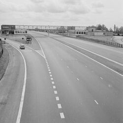 Black and white photo of an empty motorway with a glass bridge running across it.